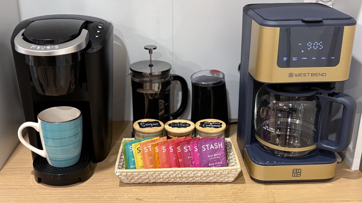 The coffee station: a Keurig, a French press, a grinder and a programmable drip coffee maker, with labeled jars of sugar, coffee and creamer and a basket of Stash teas