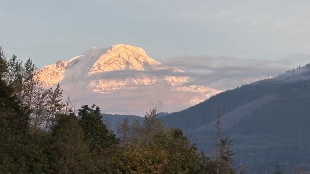 Mt. Baker’s glaciated summit glowing pink at sunset above forested ridges, seen from along Canyon Creek near the cabin